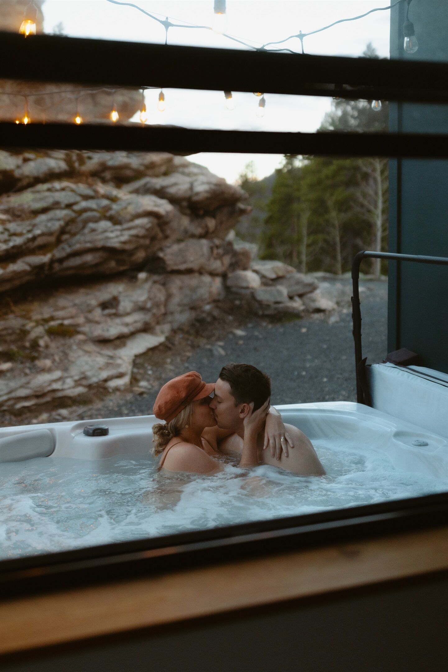 Ein Paar in einer Badewanne mit felsiger Landschaft und Bäumen im Hintergrund.