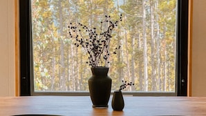 A dining table with two chairs and a vase with branches on a window sill.
