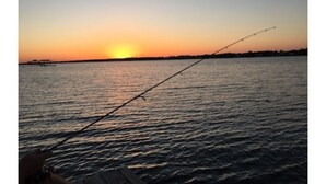 Une canne à pêche tendue au-dessus d’une étendue d’eau calme, au coucher du soleil.