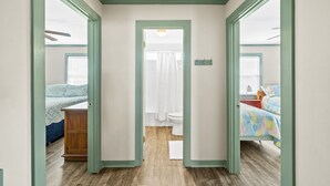 Un couloir étroit mène à une salle de bain équipée de toilettes et d’une douche.