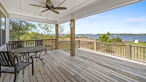Une terrasse en bois avec une table et des chaises, donnant sur une étendue d’eau, avec un kiosque visible au loin.