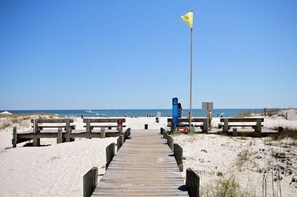 A wooden boardwalk leading to a beach with benches and a flagpole.