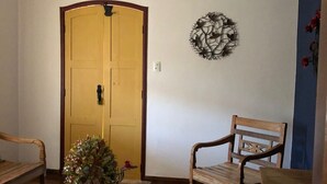 Une pièce avec une porte en bois, un élément décoratif fixé au mur et une table sur laquelle est posé un vase de fleurs.