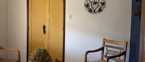 A room with a wooden door, a wall-mounted decorative piece, and a table with a vase of flowers.