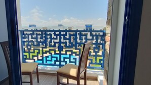 A balcony with a geometric patterned fence, two wooden chairs, and a view of modern buildings.