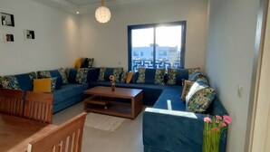 A living room with a sofa, coffee table, and chairs. There is a window with a view of buildings.