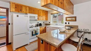A modern kitchen with wooden cabinets, a white refrigerator, a microwave, and a stove. - Bearpaw Bungalow | Fenced Yard · Near Lake (Big Bear Lake)