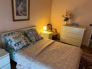Un dormitorio con cama, mesita de noche, cómoda y un cuadro en la pared.