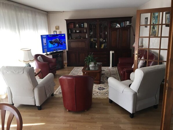 Una sala de estar con televisor, dos sillones, un reposapiés rojo, una mesa de centro y una estantería.