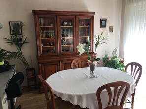 Un comedor con una mesa redonda, sillas, un aparador con puertas de cristal y plantas en macetas.