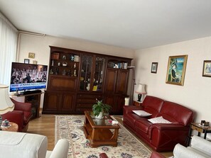 Una sala de estar con un sofá rojo, un aparador de madera, un televisor y una alfombra estampada.