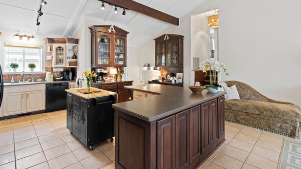 Een ruime keuken met donkere houten kastjes, een groot eiland en een zithoek met een gestreept sofa.