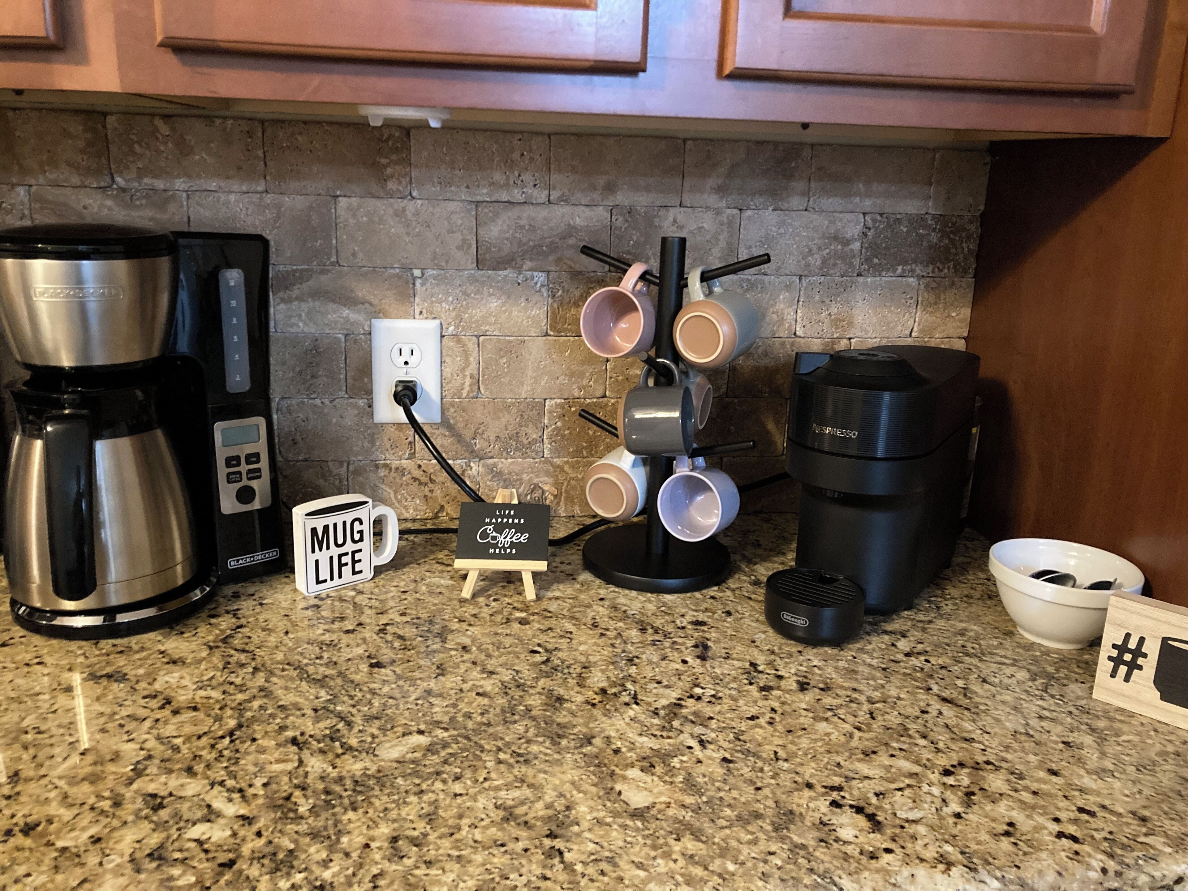A kitchen counter with a coffee maker, mug holder, and a small sign that reads "Life Happens Coffee Helps."