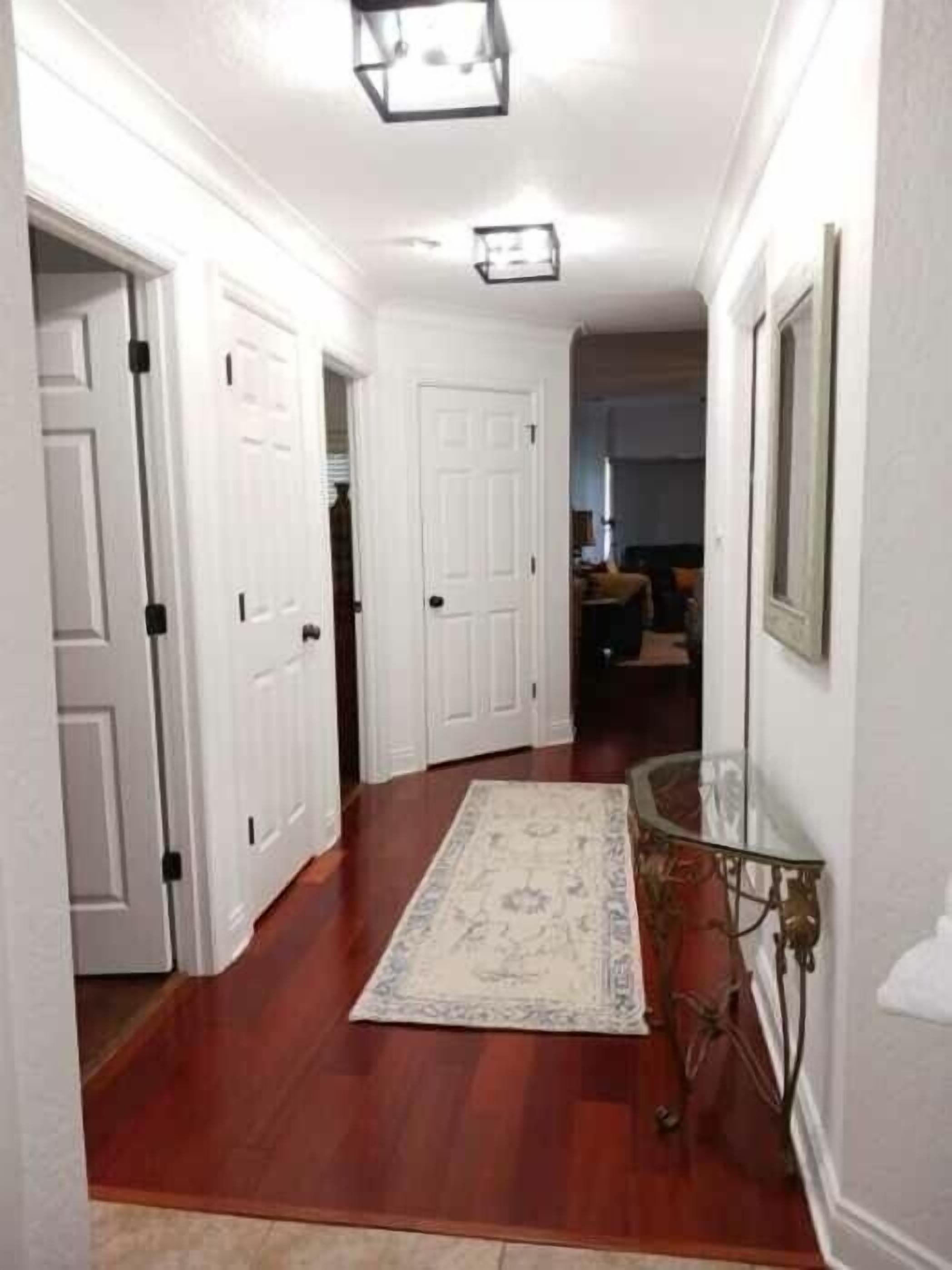 A hallway with white doors, a patterned rug, and a glass table with a red bag.