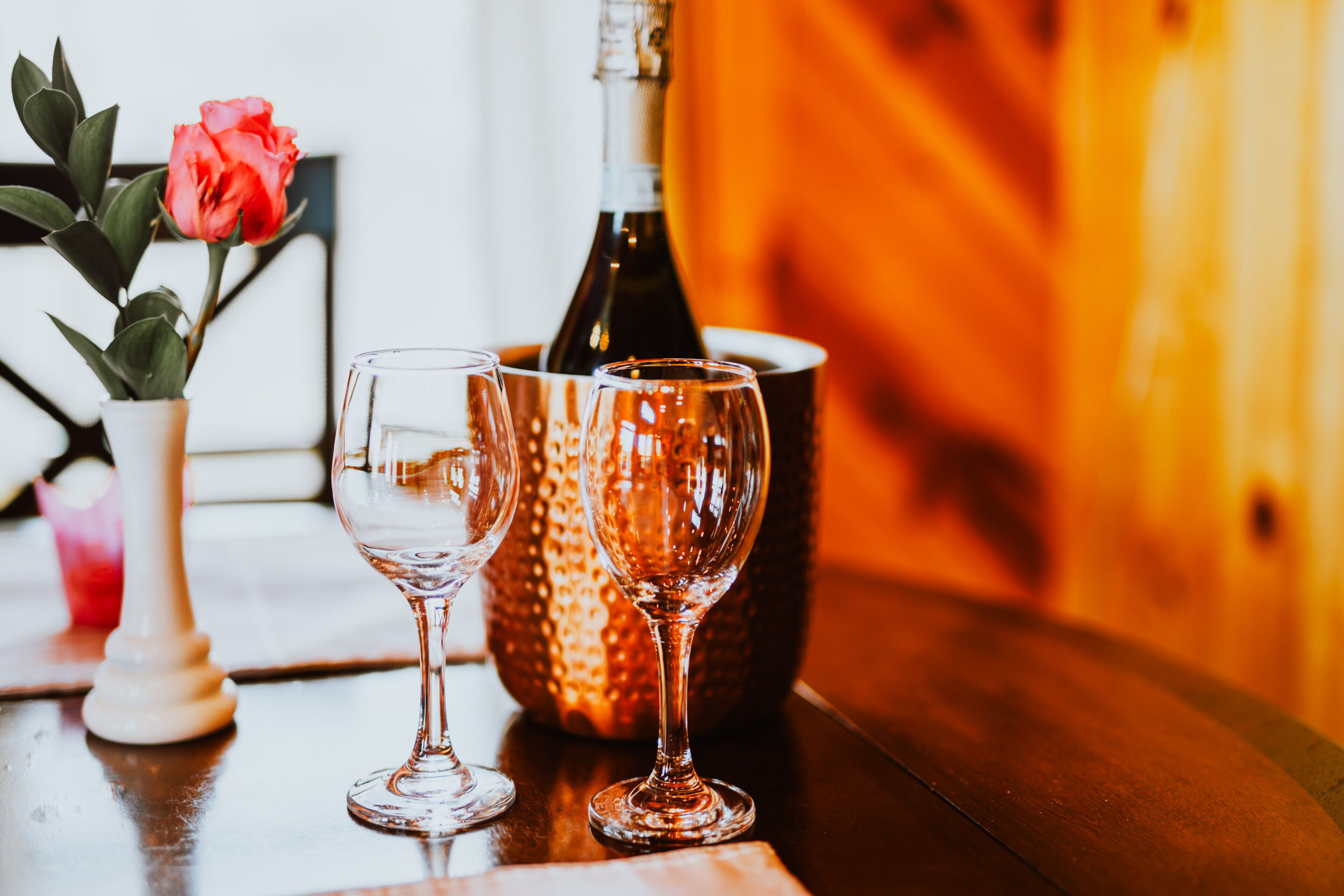 Une table avec deux verres à vin, une bouteille et un vase contenant une rose.
