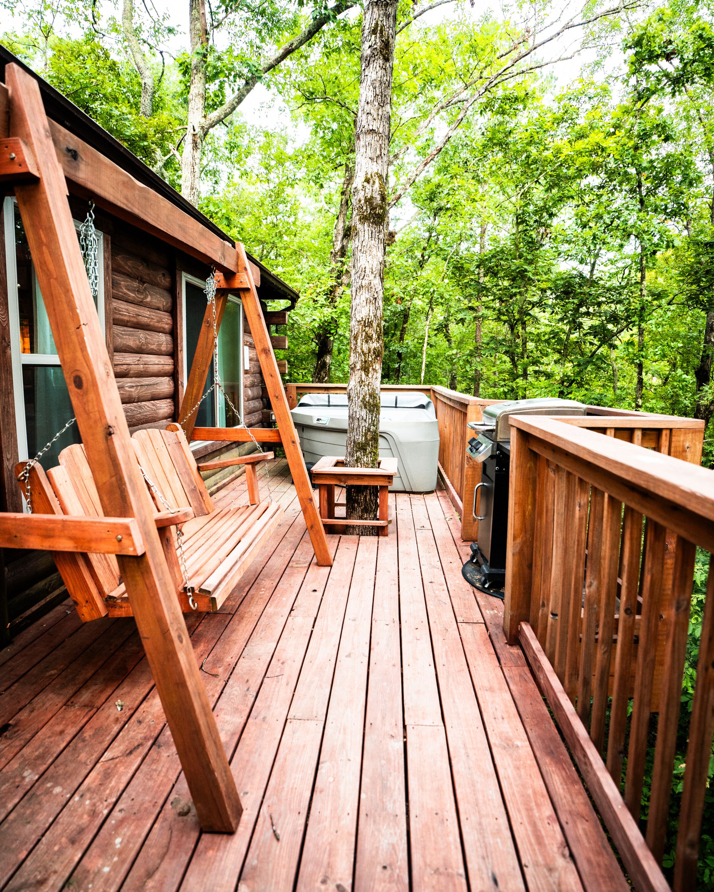 A wooden deck with a swing chair, a barbecue grill, and a hot tub.