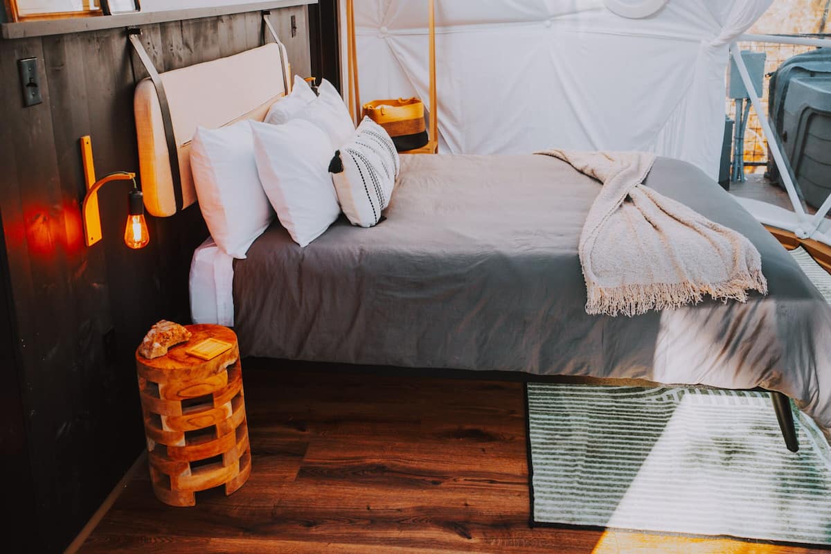 A tent-style room with a bed, wooden floor, and a small stool.
