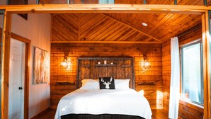 A wooden cabin bedroom with a bed, a ceiling fan, and a window. - Starlight Haven Hot Springs (Hot Springs)