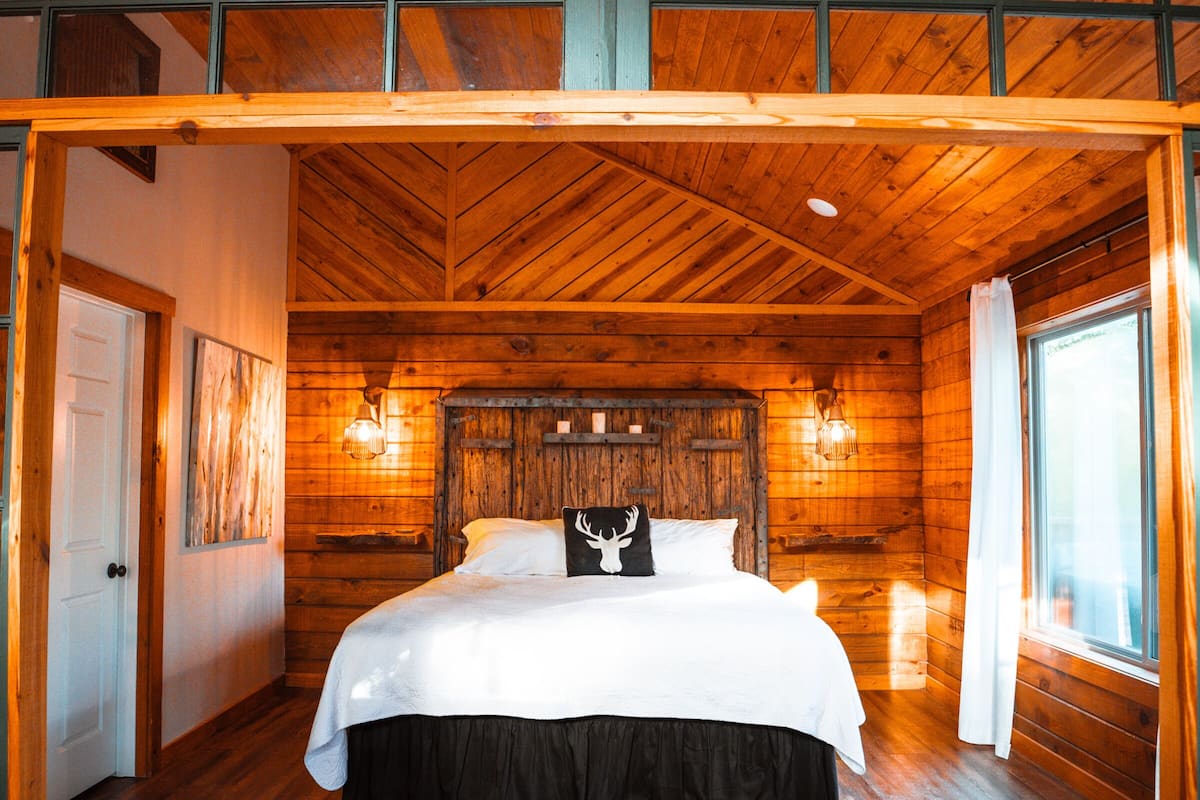 A wooden cabin bedroom with a bed, a ceiling fan, and a window.