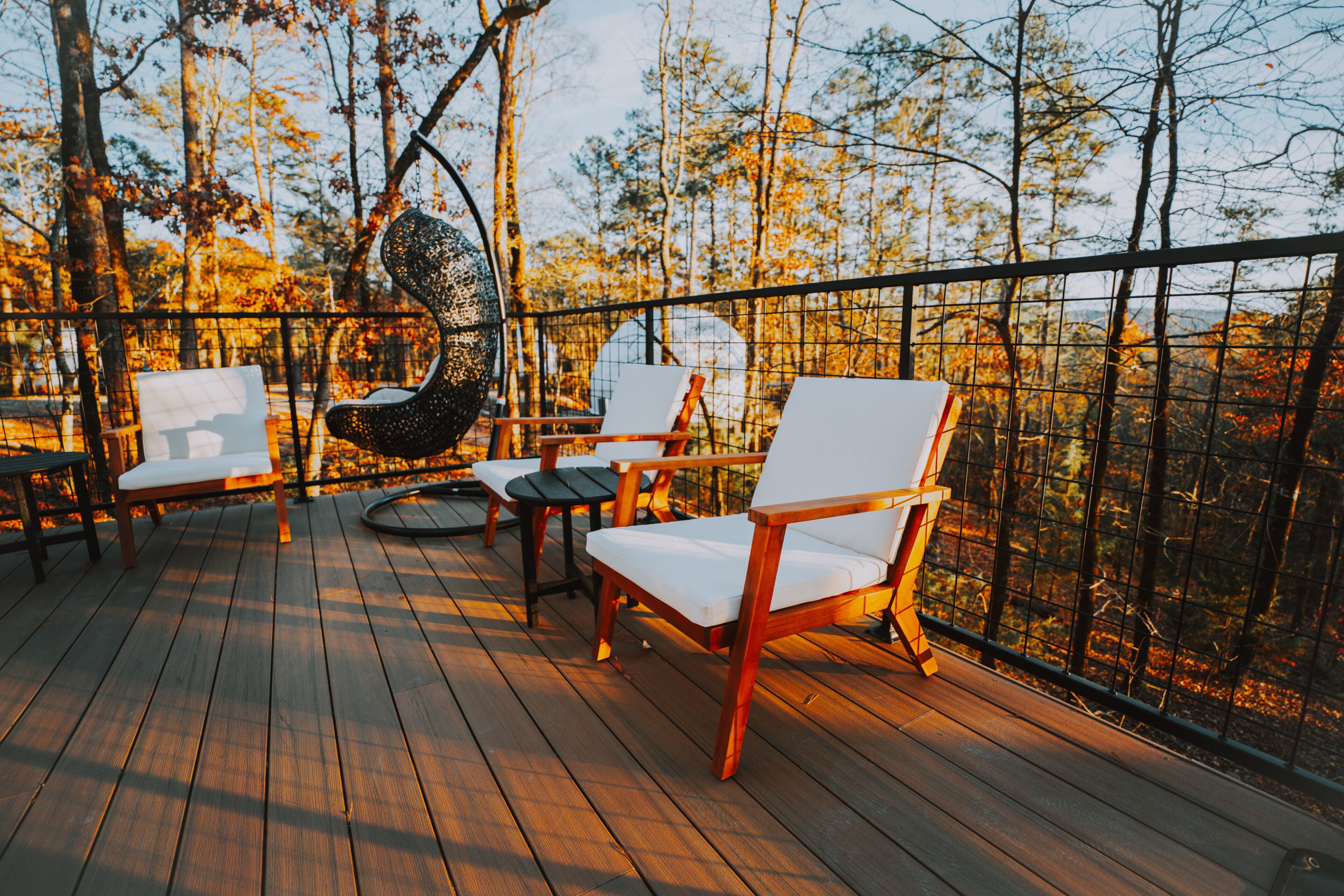 A wooden deck with outdoor seating, including chairs and a table, surrounded by a metal fence.