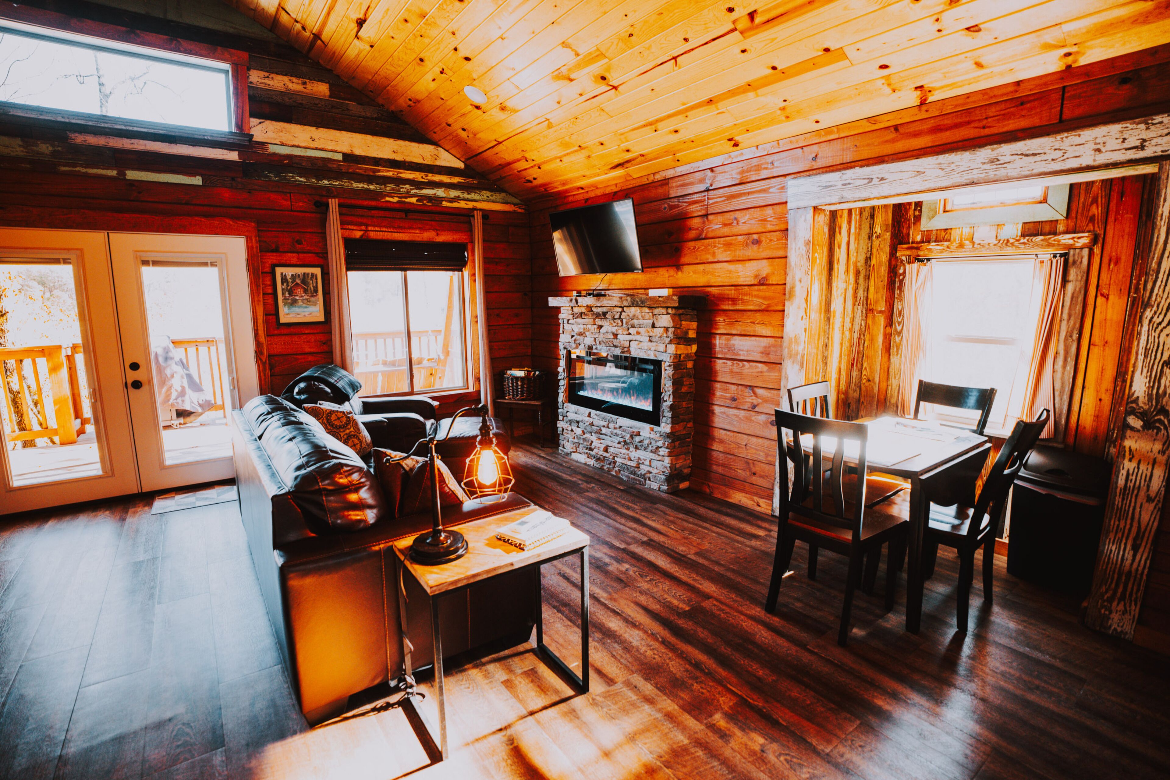 A cozy cabin interior with a stone fireplace, wooden walls, a sofa, and a dining table.