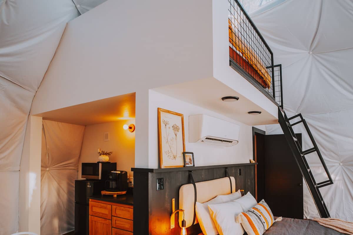 A tented accommodation with a bed, a kitchenette, and a staircase.