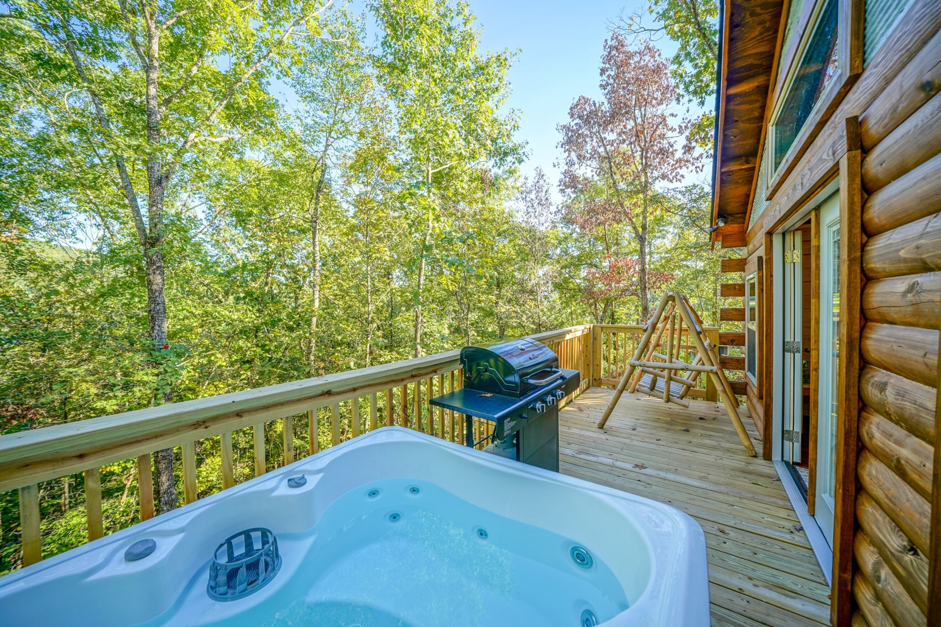 A wooden deck with a hot tub, a grill, and a ladder.