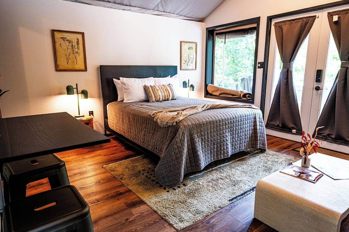 A bedroom with a bed, a desk, and a window with curtains.