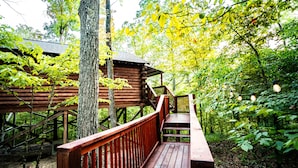 A wooden cabin with a wooden deck and stairs leading up to it, surrounded by trees and greenery. - Starlight Haven Hot Springs (Hot Springs)