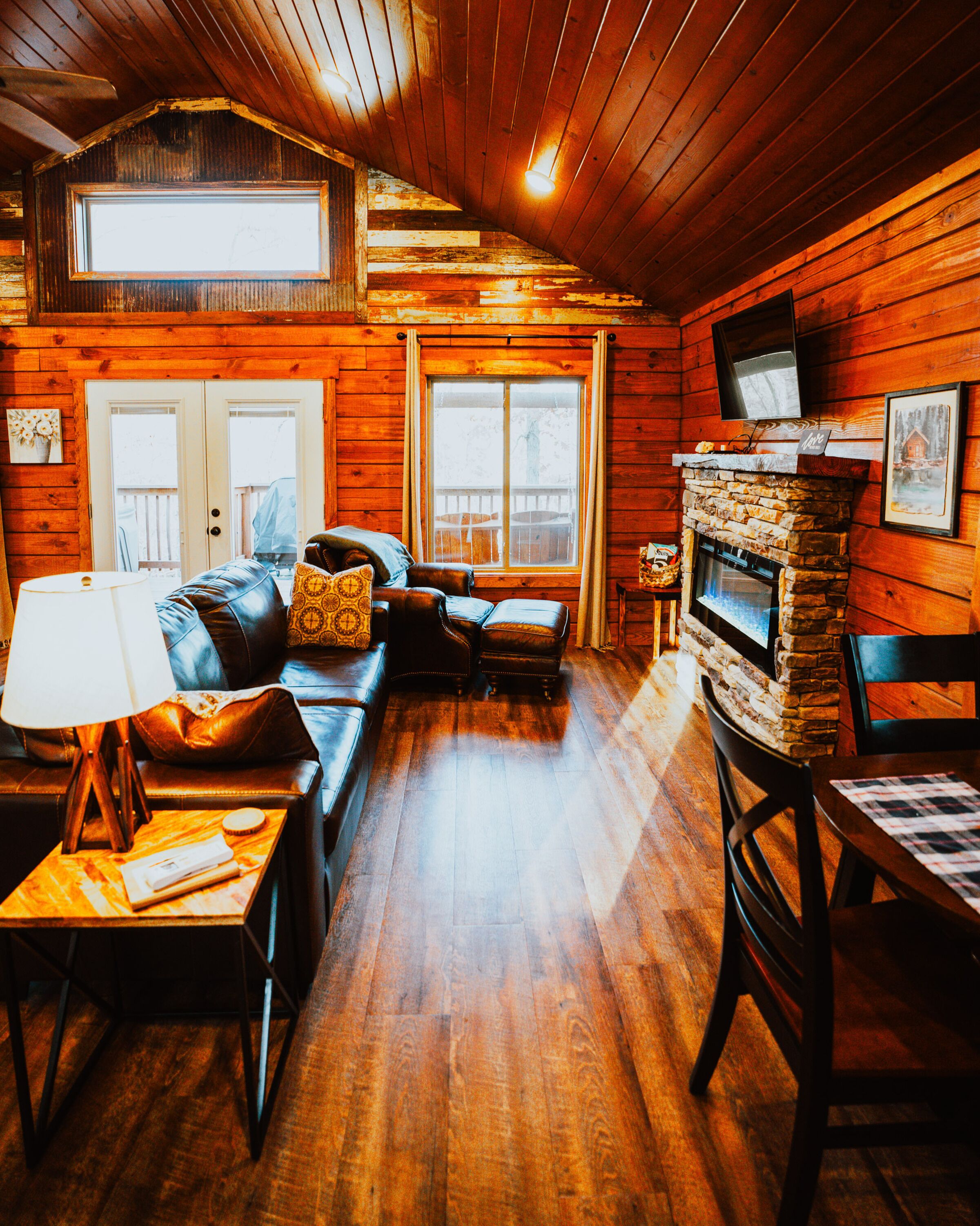 A cozy cabin interior with a stone fireplace, wooden walls, a sofa, and a dining table.
