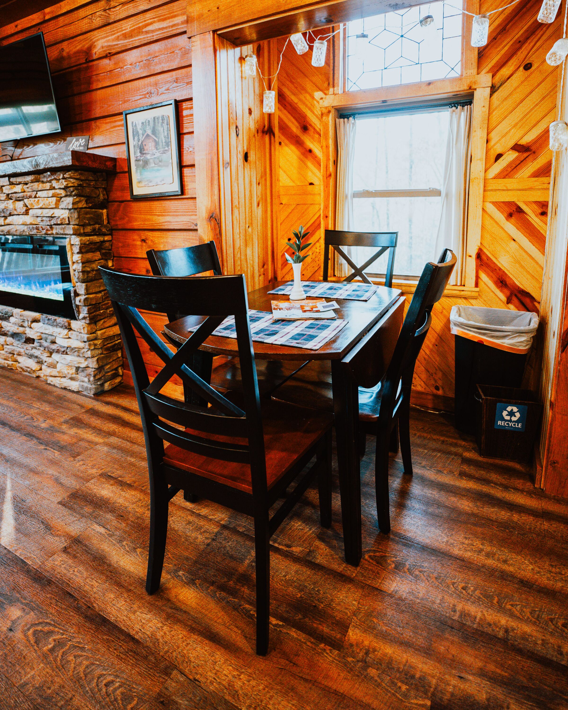 A wooden interior with a stone fireplace, a dining table with chairs, and a television mounted on the wall.