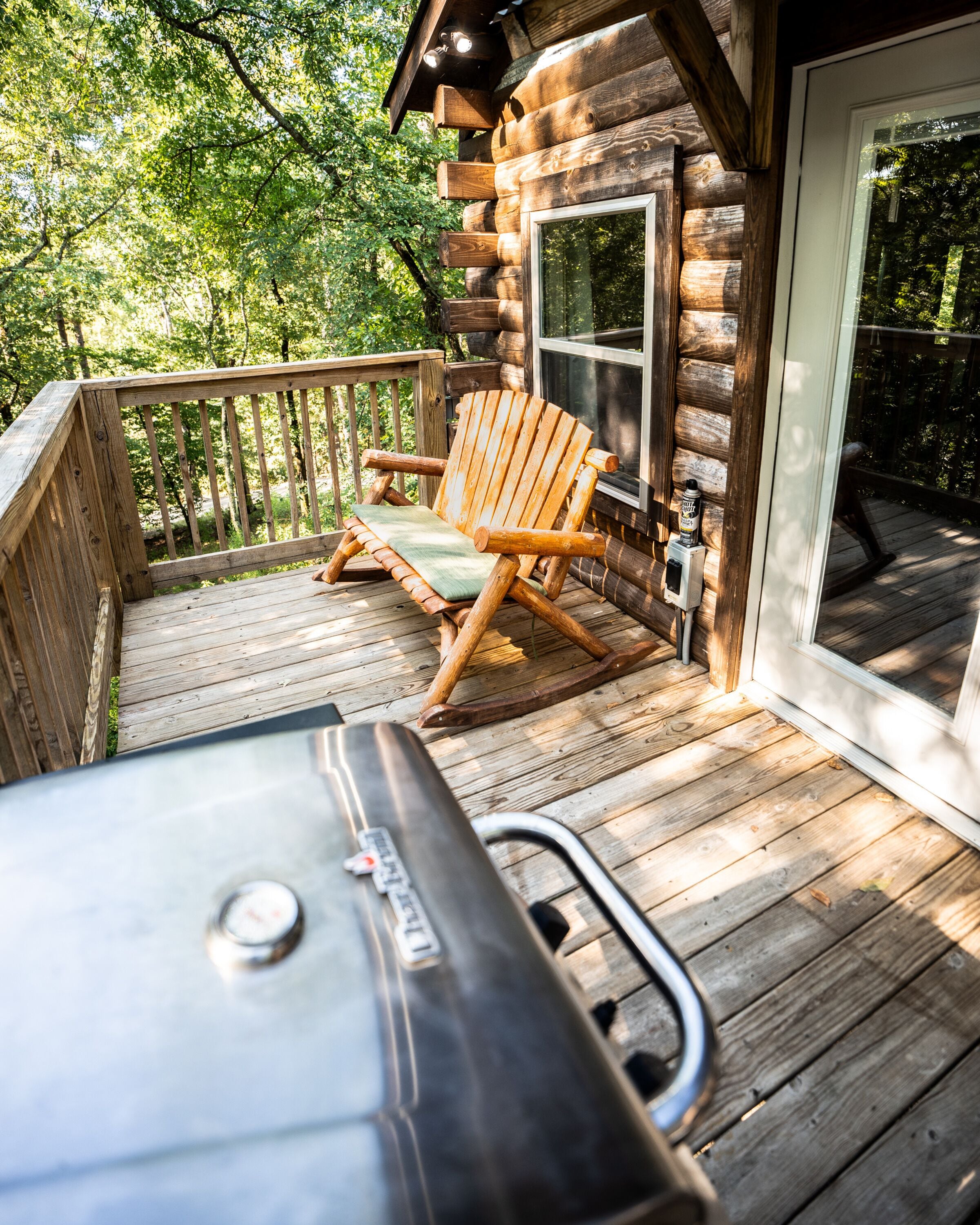 A wooden deck with a grill, a wooden Adirondack chair, and a glass door leading to a covered area.