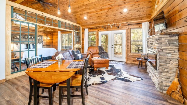 A spacious room with a wooden ceiling, a dining area with a table and chairs, a leather sofa, and a stone fireplace. - Starlight Haven Hot Springs (Hot Springs)