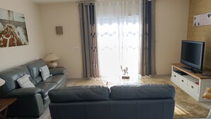 A living room with a sofa, a television on a stand, a lamp, and a painting on the wall. - Beautiful house near the ocean—peaceful, charming, and perfect for a family vacation (Meschers-sur-Gironde)