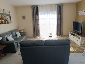 Ein Wohnzimmer mit einer Couch, einem Fernseher auf einem Schrank, einer Lampe und einem Gemälde an der Wand.