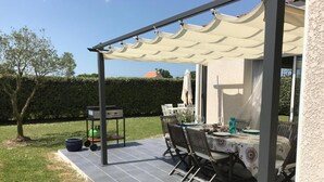 An outdoor patio with a table and chairs, a grill, and a covered area with a pergola. - Beautiful house near the ocean—peaceful, charming, and perfect for a family vacation (Meschers-sur-Gironde)