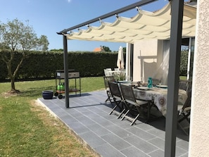 Eine Terrassengaststätte mit Tisch und Stühlen, einem Grill und einem überdachten Bereich mit einer Pergola.