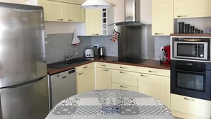 A modern kitchen with stainless steel appliances, a round dining table, and light-colored cabinetry. - Beautiful house near the ocean—peaceful, charming, and perfect for a family vacation (Meschers-sur-Gironde)