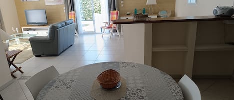 A modern living room with a sofa, a television, and a dining area with a table and chairs.