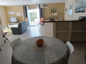 A modern living room with a sofa, a television, and a dining area with a table and chairs. - Beautiful house near the ocean—quiet, charming, and perfect for a family vacation (Meschers-sur-Gironde)