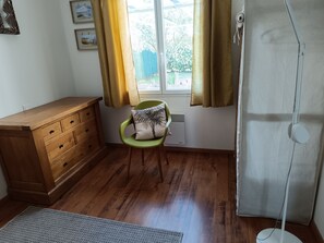 A room with a wooden dresser, a green chair with a pillow, a radiator, and a window with curtains.