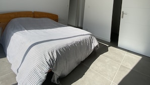 Ein Schlafzimmer mit einem Bett, einem Holzkopfende, einer weißen Tür und einem gefliesten Boden.