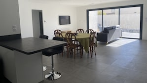 Eine moderne Küche mit Bar, Esstisch und Stühlen. Ein Fernseher ist an der Wand befestigt und eine Glastür führt in einen Außenbereich.