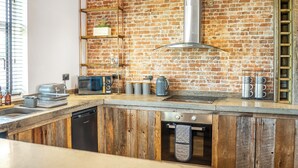 A kitchen with a brick wall, wooden cabinets, a stainless steel range hood, and a built-in oven.