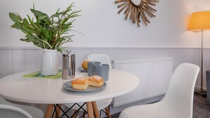 A dining area with a round table, white chairs, a potted plant, a decorative mirror, and a lamp. - Salty Dog Apartment @ Sunnybeach (Paignton)