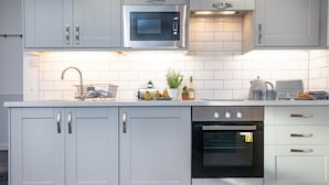 A modern kitchen with white cabinetry, a built-in oven, a microwave, and a dish rack with dishes. - Anchors Away Apartment @ Sunnybeach (Paignton)