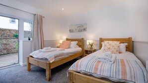 A bedroom with two wooden beds, each with a striped blanket and pillows, a small bedside table with a lamp, and a painting on the wall. - Anchors Away Apartment @ Sunnybeach (Paignton)