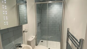 Moderni kylpyhuone, jossa on lasinen suihkuseinä, valkoinen pesuallas ja wc-istuin.