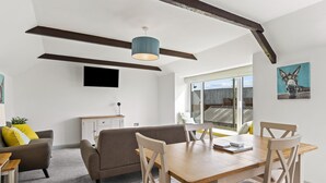 Ein stilvoller Essbereich mit einem Holztisch und -stühlen, einem grauen Sofa und einem Deckenventilator.