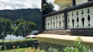 A traditional building with a balcony overlooking a lake, surrounded by lush greenery.